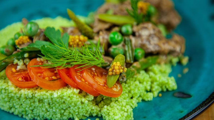 Close-up of a colorful green couscous salad with tomatoes and fresh herbs.